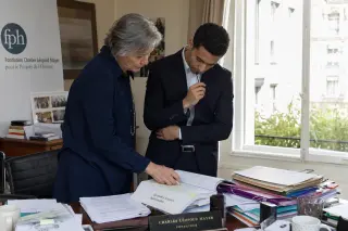 Overhead view of a wooden table with legal papers and reports, a notebook with handwritten notes, a hand marking a statute booklet, soft natural light, evoking thoughtful preparation for a philanthropic foundation.